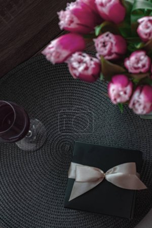 Photo for Bouquet of beautiful spring flowers, red tulips, one glass of aromatic red wine and black present box with ribbon. Woman day - Royalty Free Image