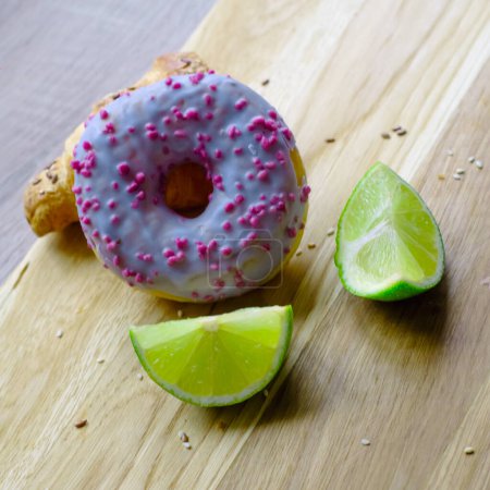 juicy two halfs of green lime and one big round violet glazed donut on wooden tray. Eat concepts. GMO free