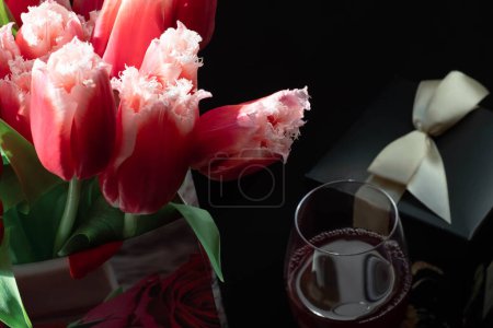 Photo for Bouquet of beautiful spring flowers, red tulips, one glass of aromatic red wine and black present box with ribbon. Woman day - Royalty Free Image