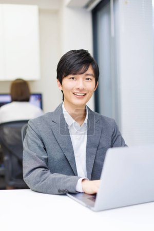 Schöner Japaner, der im Büro an einem Laptop arbeitet.