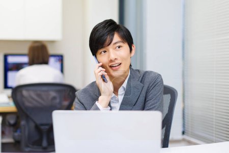 Young Japanese businessman talking on the phone while working in the office.