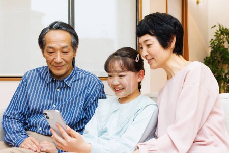 Téléchargez les photos : Famille heureuse avec téléphone intelligent sur le canapé à la maison - en image libre de droit