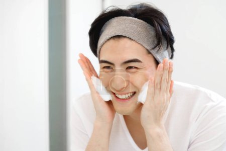 Foto de Retrato de joven japonés guapo lavándose la cara durante la rutina de la mañana en casa - Imagen libre de derechos
