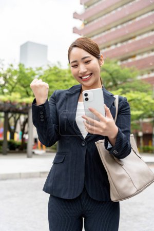 Photo for Portrait of beautiful japanese businesswoman in suit using mobile phone on the street - Royalty Free Image