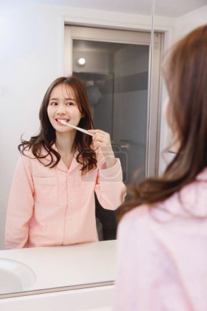 Téléchargez les photos : Femme se brossant les dents dans la salle de bain le matin - en image libre de droit
