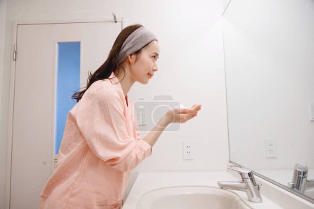Foto de Retrato de hermosa joven japonesa lavándose la cara durante la rutina de la mañana en casa - Imagen libre de derechos