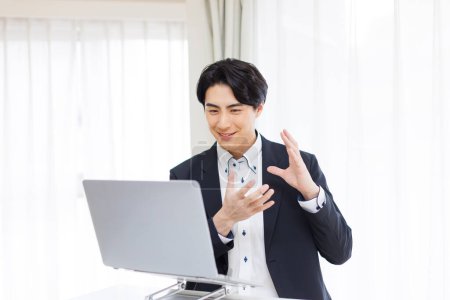 Téléchargez les photos : Un homme en costume est assis à une table avec un ordinateur portable ayant un appel vidéo - en image libre de droit