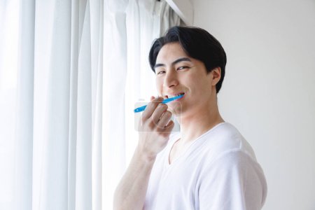 Téléchargez les photos : Portrait de beau jeune Japonais brossant des dents à la maison - en image libre de droit
