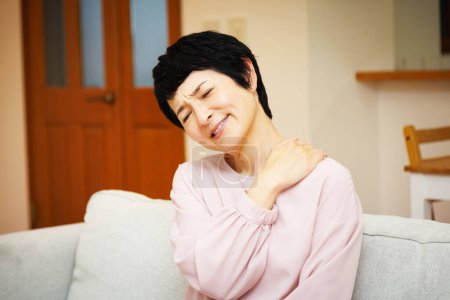 Téléchargez les photos : Asiatique femme avec épaule douleur à la maison - en image libre de droit