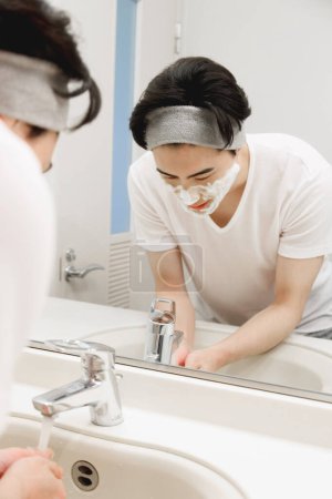 Foto de Retrato de joven japonés guapo lavándose la cara durante la rutina de la mañana en casa - Imagen libre de derechos