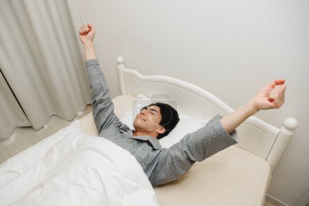 Téléchargez les photos : Portrait de beau jeune Japonais couché dans son lit à la maison - en image libre de droit