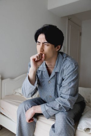 Photo for Portrait of handsome young Japanese man having cough while sitting on bed - Royalty Free Image