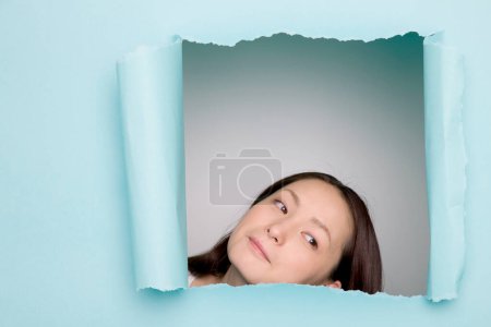 Foto de Retrato de una mujer japonesa mirando a través de un agujero en papel azul roto - Imagen libre de derechos