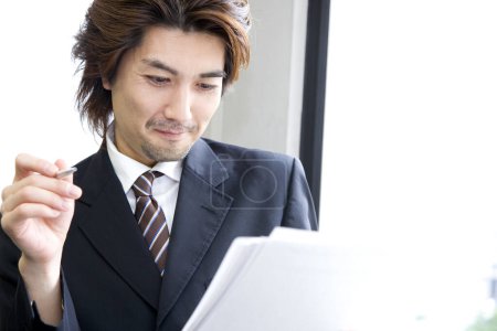 Foto de Joven asiático hombre de negocios leyendo documentos en oficina - Imagen libre de derechos