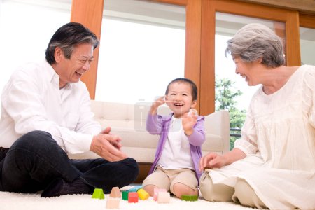 asiatische Familie Großvater und Großmutter spielen mit ihrem Enkel auf dem Boden mit Holzwürfeln