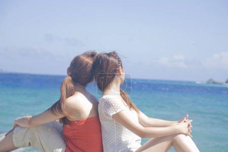 Téléchargez les photos : Vue arrière de la mère et de la fille assises sur la plage - en image libre de droit