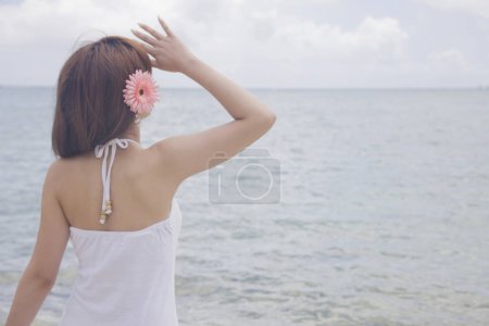 Foto de Vista trasera de mujer asiática con flor rosa en el pelo disfrutando de vista al mar - Imagen libre de derechos