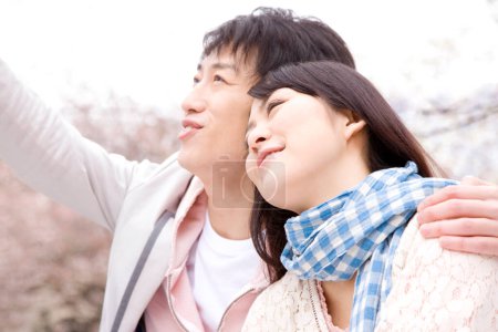 Photo for Portrait of happy young japanese couple spending time together in park during sakura blossom - Royalty Free Image