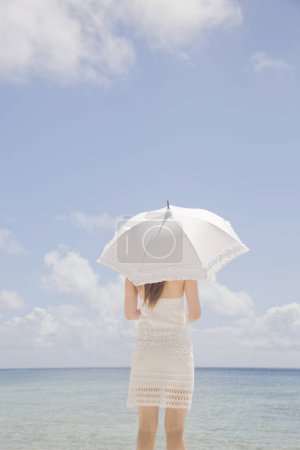 Foto de Mujer con paraguas blanco de pie en la playa de verano, vista trasera - Imagen libre de derechos