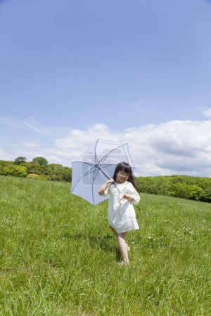 Foto de Lindo poco asiático chica con paraguas en verde campo - Imagen libre de derechos