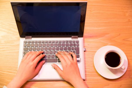 Téléchargez les photos : Mains féminines tapant sur le clavier de l'ordinateur portable avec tasse de café. vue de dessus. - en image libre de droit