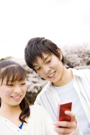Téléchargez les photos : Young japanese couple making selfie during walking at cherry trees garden - en image libre de droit
