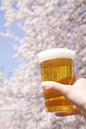 Téléchargez les photos : Main tenant un verre de bière sur le fond du jardin de printemps - en image libre de droit