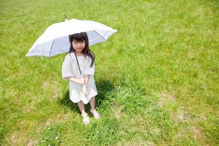 Téléchargez les photos : Mignonne petite fille asiatique avec parapluie sur champ vert - en image libre de droit