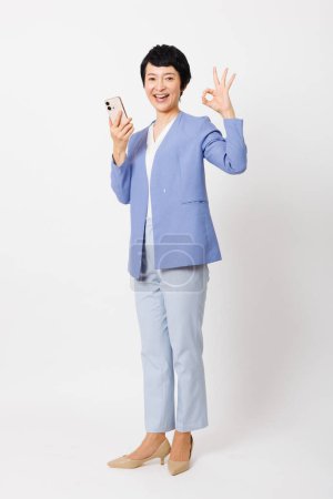 Foto de Retrato de asiático senior mujer usando inteligente teléfono mostrando ok aislado en blanco fondo - Imagen libre de derechos