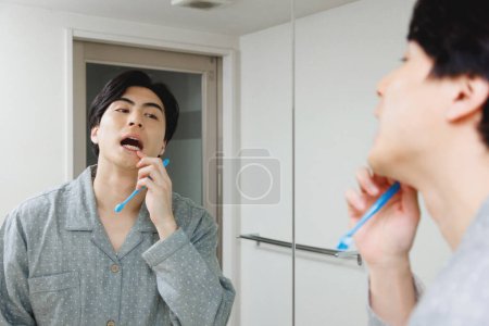 Foto de Retrato de guapo joven japonés hombre cepillarse los dientes en casa - Imagen libre de derechos