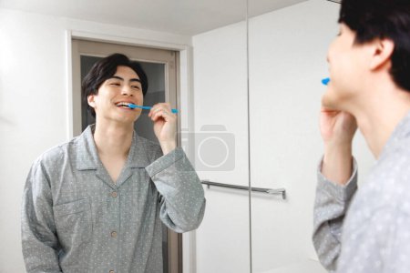Foto de Retrato de guapo joven japonés hombre cepillarse los dientes en casa - Imagen libre de derechos