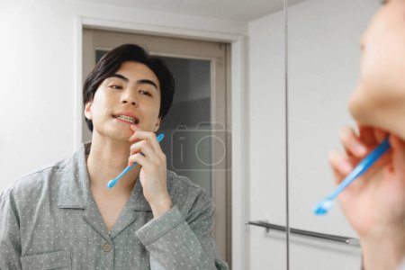 Téléchargez les photos : Portrait de beau jeune Japonais brossant des dents à la maison - en image libre de droit