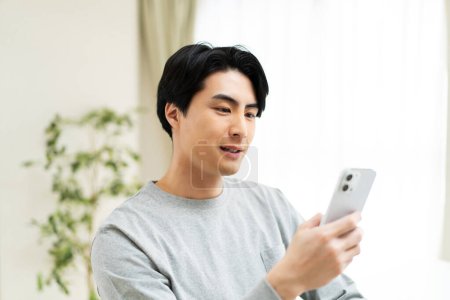 Téléchargez les photos : Jeune asiatique homme en utilisant smartphone - en image libre de droit