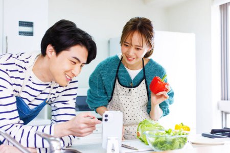 Téléchargez les photos : Asiatique homme et femme cuisine dans cuisine, en utilisant le téléphone pour la recette - en image libre de droit