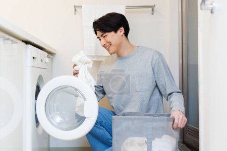 Téléchargez les photos : Jeune homme mettre la lessive dans la machine à laver - en image libre de droit