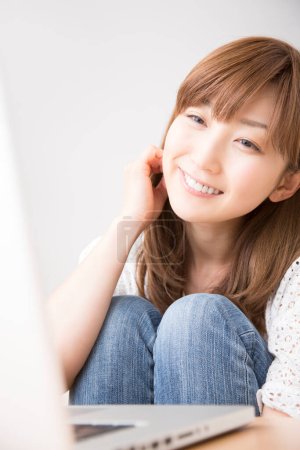 Téléchargez les photos : Belle femme japonaise souriante avec ordinateur portable à la maison - en image libre de droit