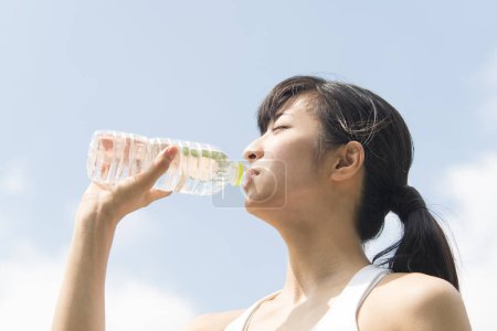 Photo for Beauty Japanese woman drinking water during jogging in summer park - Royalty Free Image