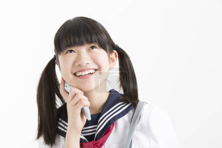 Téléchargez les photos : Portrait de belle jeune étudiante en uniforme scolaire avec téléphone portable sur fond blanc - en image libre de droit