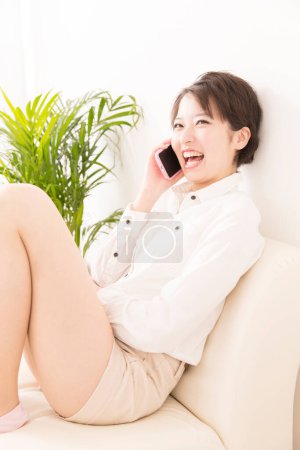 Photo for Beautiful young Japanese woman talking to cell phone in the living room - Royalty Free Image