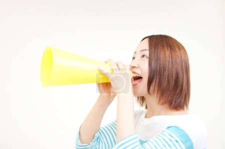 Téléchargez les photos : Portrait de belle jeune femme japonaise criant avec haut-parleur sur fond beige - en image libre de droit
