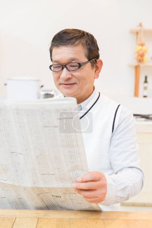 Téléchargez les photos : Portrait de mature asiatique homme lecture journal à la maison - en image libre de droit