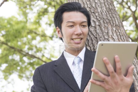 Photo for Asian businessman with tablet pc in park - Royalty Free Image