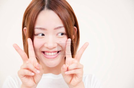 Porträt der schönen jungen Japanerin mit V-Zeichen auf beigem Hintergrund