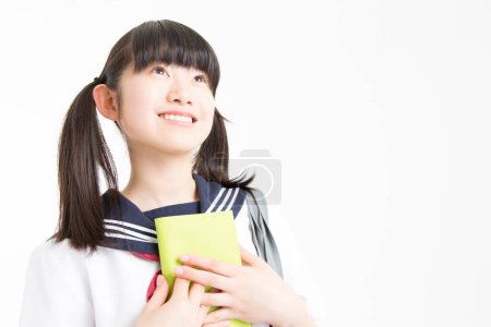 Téléchargez les photos : Portrait de belle jeune étudiante en uniforme scolaire avec livre sur fond blanc - en image libre de droit