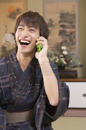 retrato de joven japonés guapo en yukata tradicional usando teléfono inteligente en hotel de aguas termales étnicas