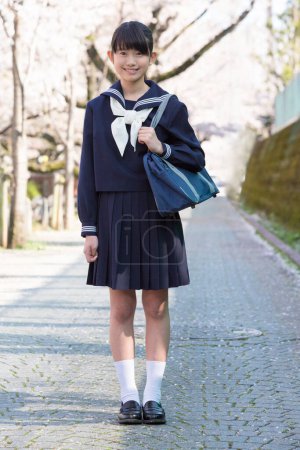 Photo for Portrait of beautiful Japanese student on street with blooming cherry trees - Royalty Free Image
