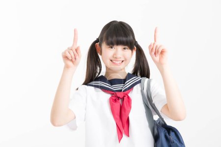 Téléchargez les photos : Portrait de belle jeune étudiante en uniforme scolaire pointant sur fond blanc - en image libre de droit