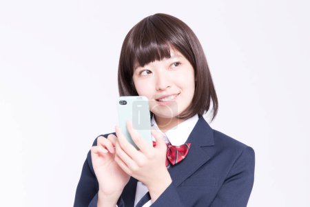 Téléchargez les photos : Portrait studio d'écolière japonaise souriante utilisant un smartphone - en image libre de droit