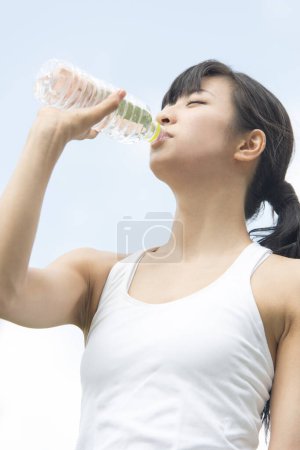 Téléchargez les photos : Beauté femme japonaise boire de l'eau pendant le jogging dans le parc d'été - en image libre de droit