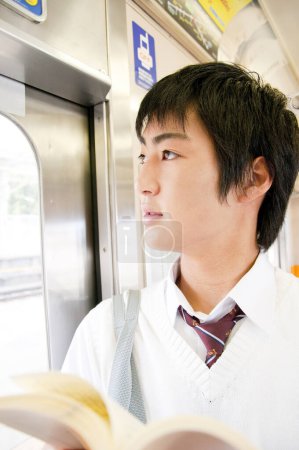 Photo for Japanese student boy reading a book in train - Royalty Free Image